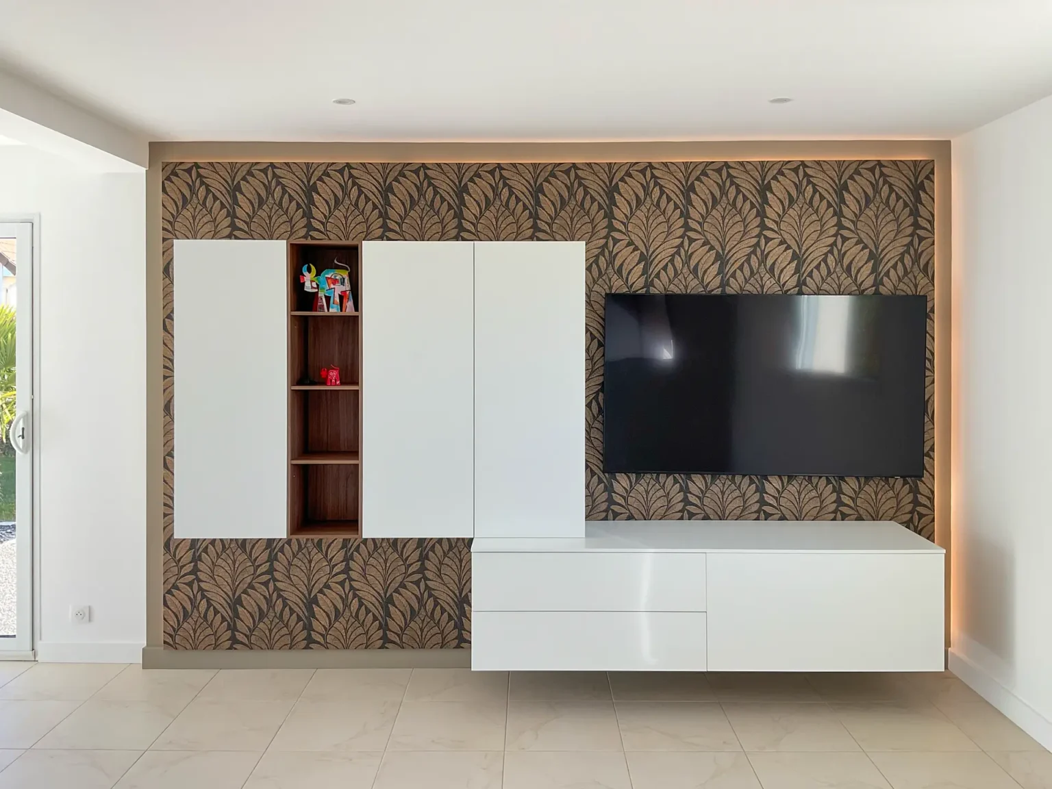 Mur TV sur-mesure : colonnes laquées blanches, niche en bois et rétroéclairage sur papier peint feuillage