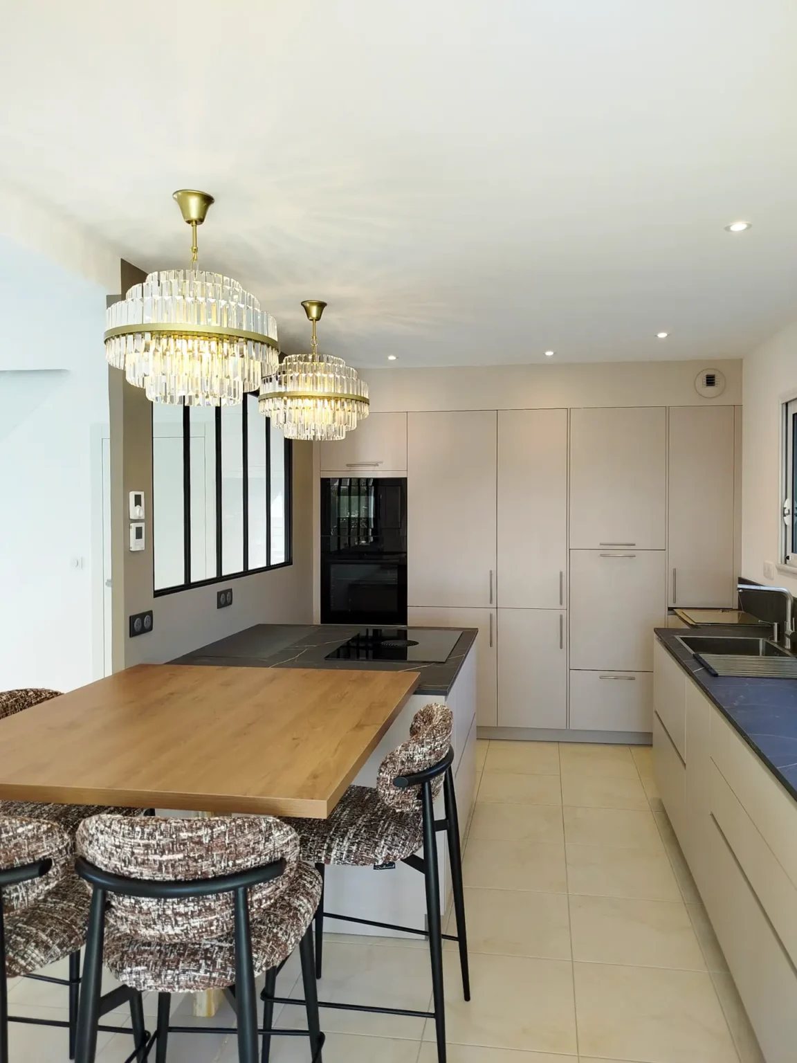 Cuisine rénovée à Gavrus : îlot en chêne et chaises tapissées, colonnes beige et lustres en cristal