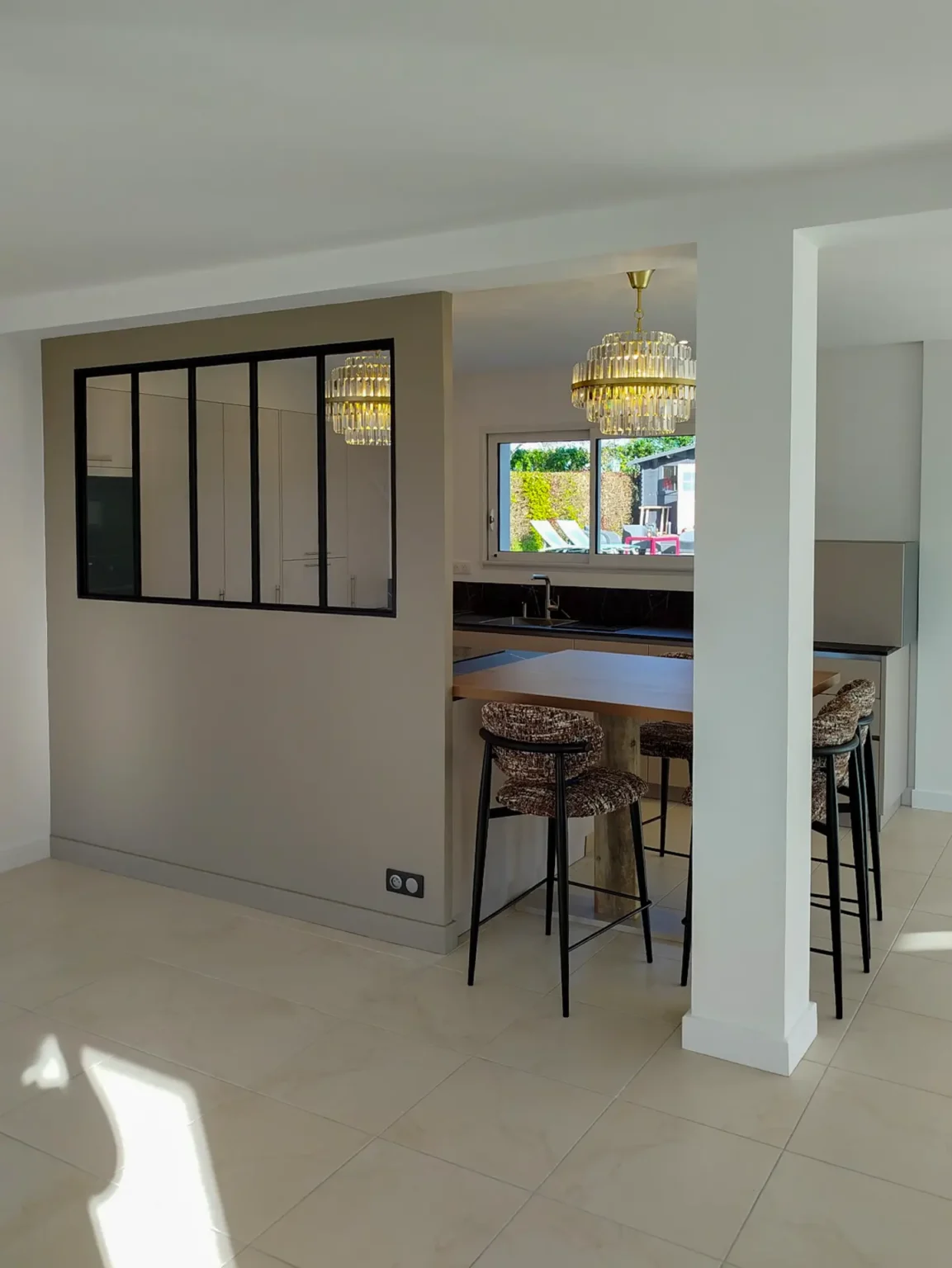 Cloison à verrière noire entre l'entrée et la cuisine, coin bar avec tabourets en arrière-plan